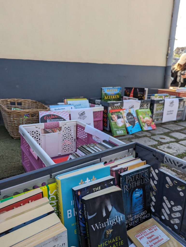 Diverse Bücher stehen in und vor Kisten auf dem Boden